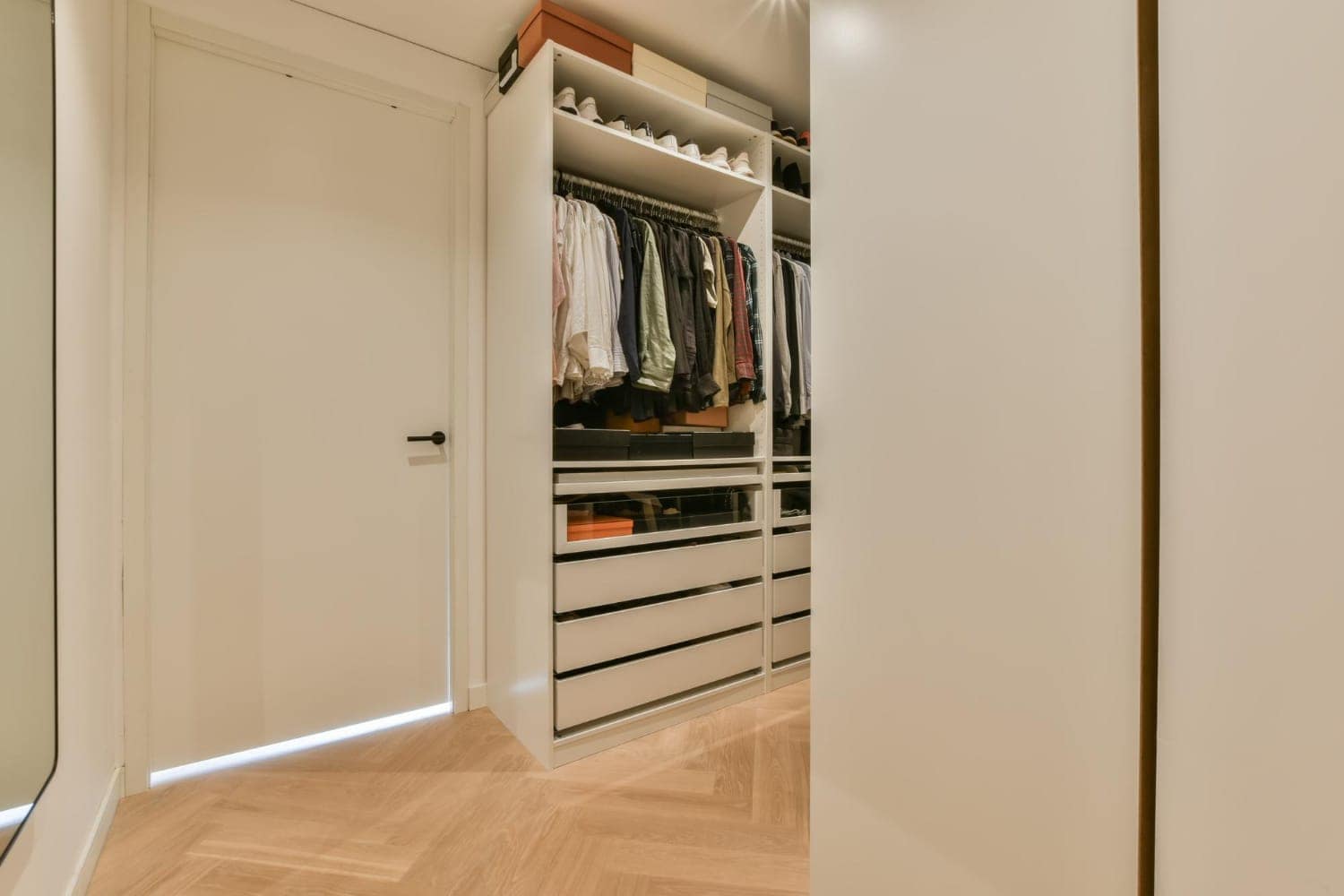 White built-in hanging and drawer unit, with clothes on a rod, stacked drawers, and shoes on the shelf above.