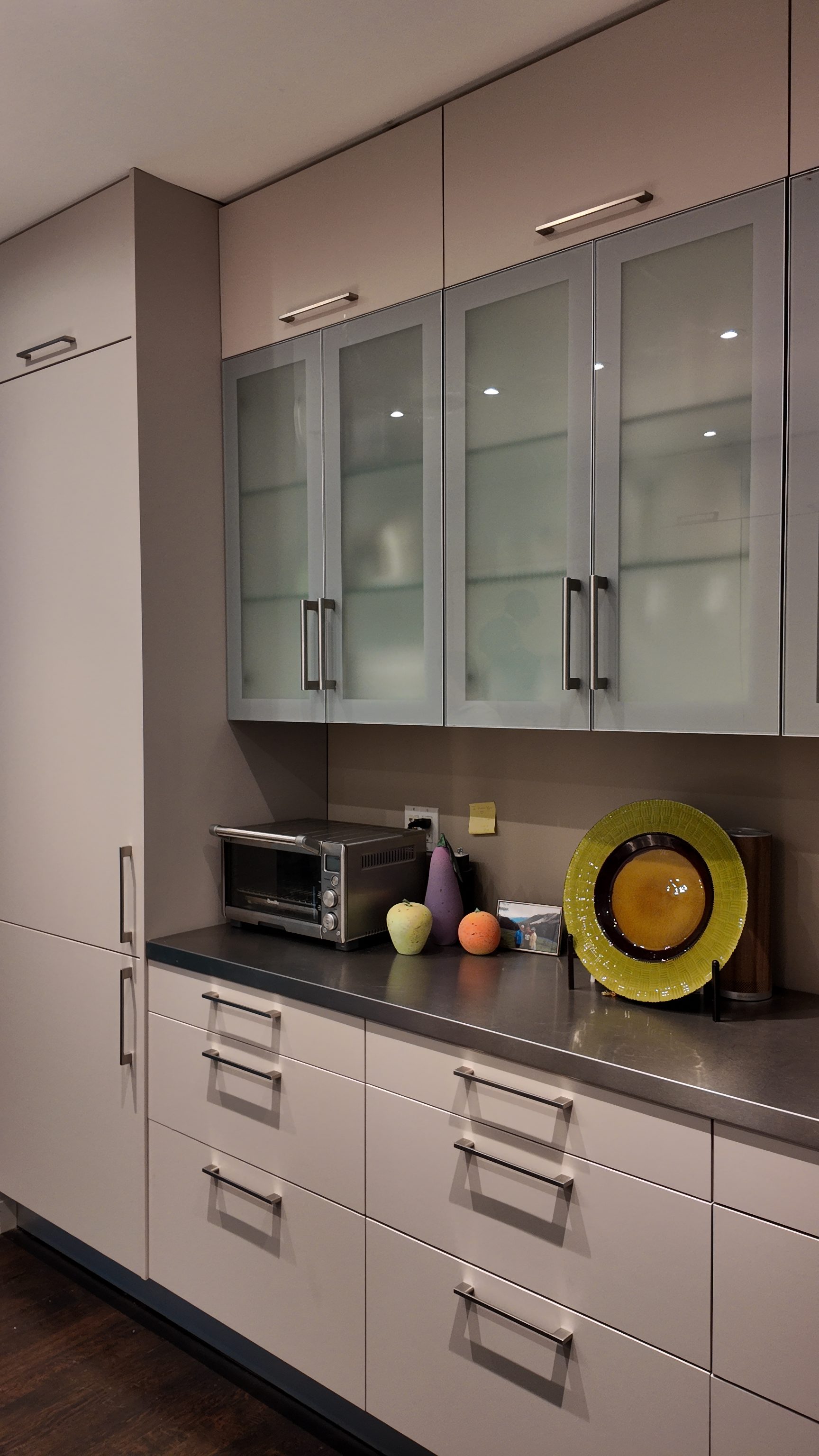 Glass-front upper cabinets with recessed pulls and integrated refrigerator panel.